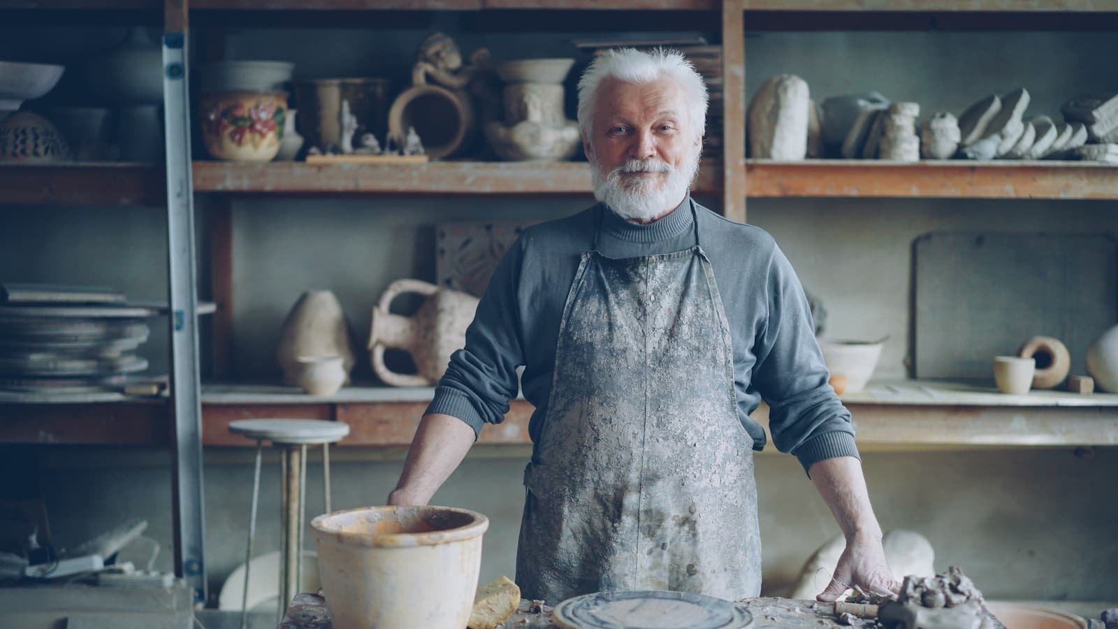 A potter shaping clay at a wheel in a workshop